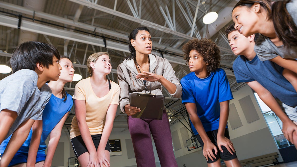 Coach talking to group of kids in gymnasium