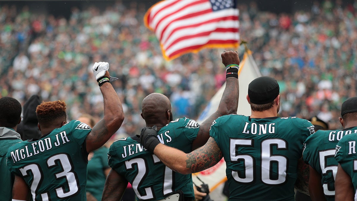 Rodney McLeod and Malcolm Jenkins raise their fists in protest while Chris Long of the Philadelphia Eagles puts arms around teammates in support 