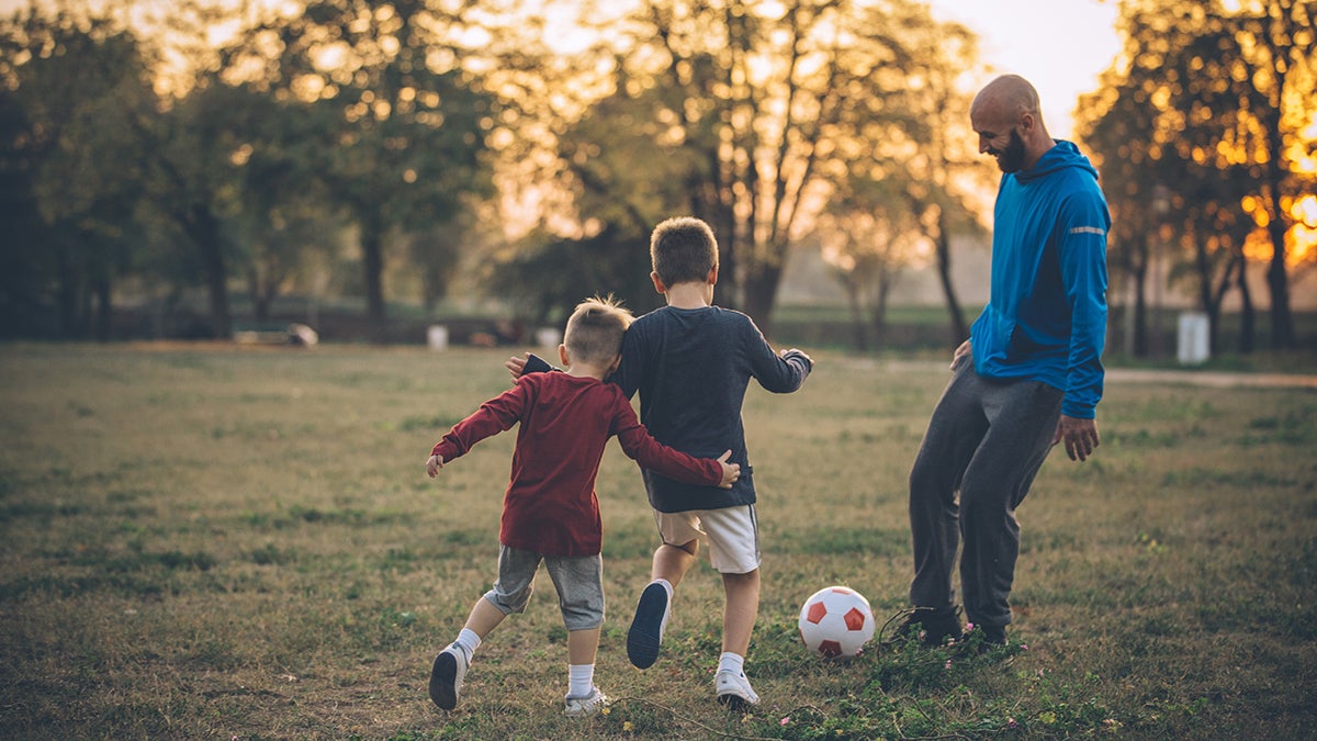 Dad playing soccer with his two sons in the fall