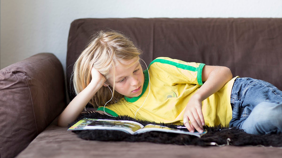 boy listening to audiobook with headphones on couch is an example of U.S. child inactivity