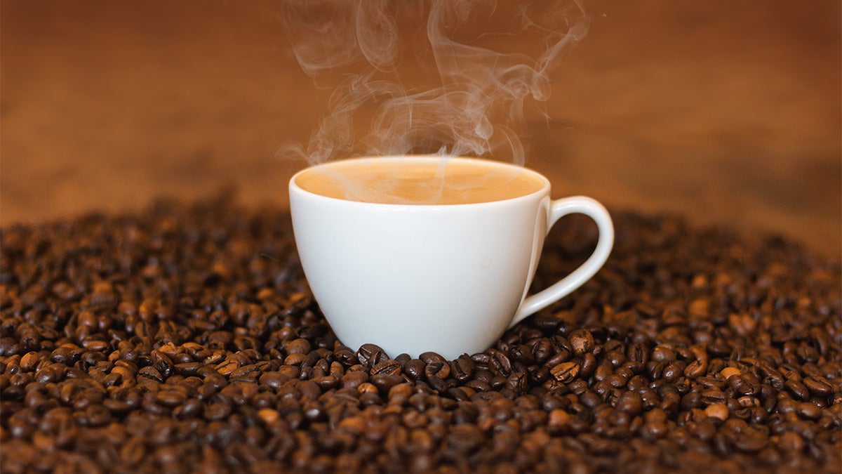 Cup of steaming coffee resting on coffee beans 