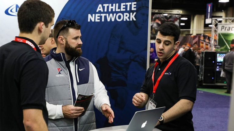 Convention where workers are showing someone a laptop at a Athlete Network booth