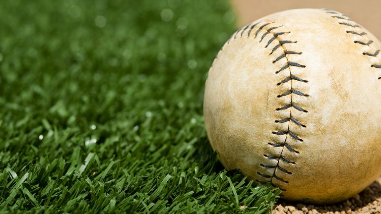 An Old Softball sitting between the infield grass and dirt of a softball diamond