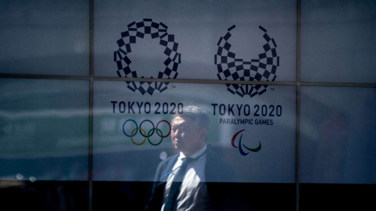 People walk past a screen showing logo the Tokyo 2020 Olympic Games and Tokyo 2020 Paralympic Games after the announcement of the games postponement to the summer of 2021. Japan, March 24, 2020. (Photo by Alessandro Di Ciommo/NurPhoto via Getty Images)