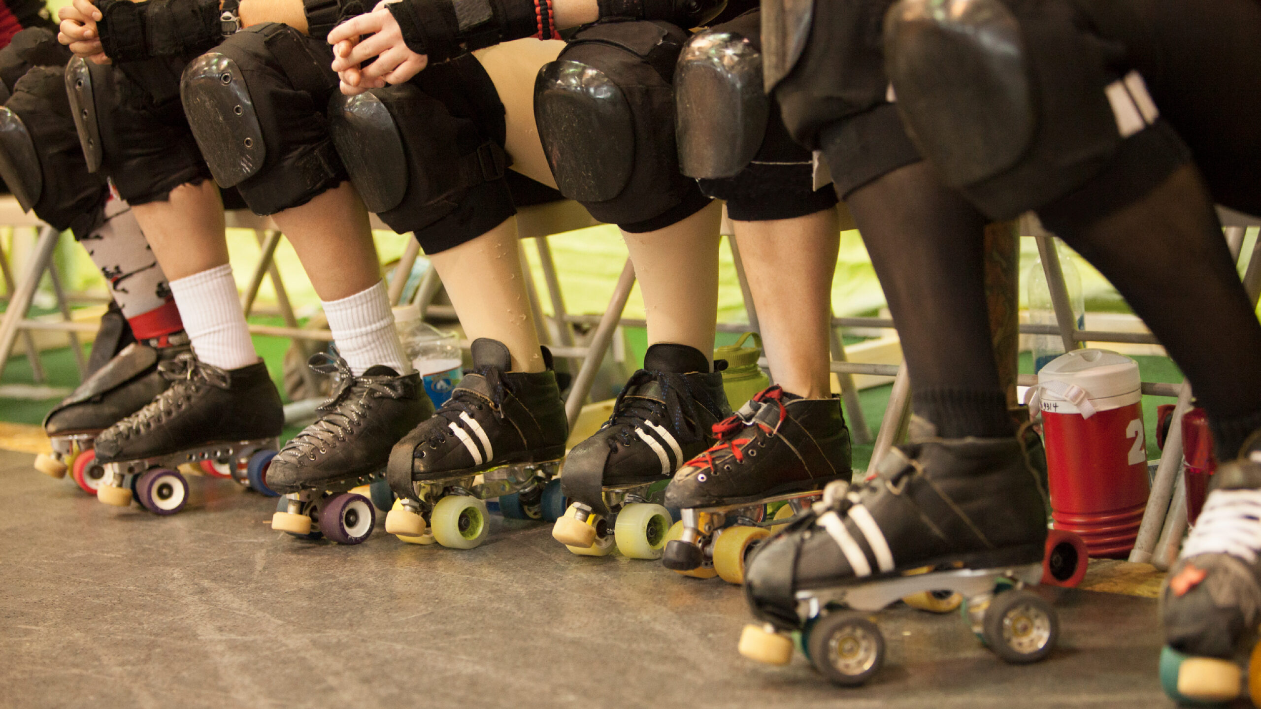 Photo of roller derby players knees, knee pads and in roller skates, seated in a row.