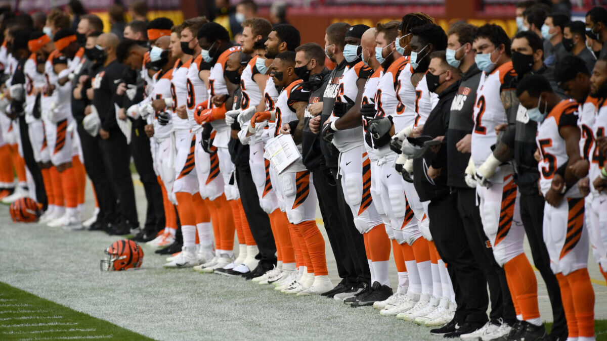 Cincinatti Bengals team lock arms on the sidelines of football field while wearing masks