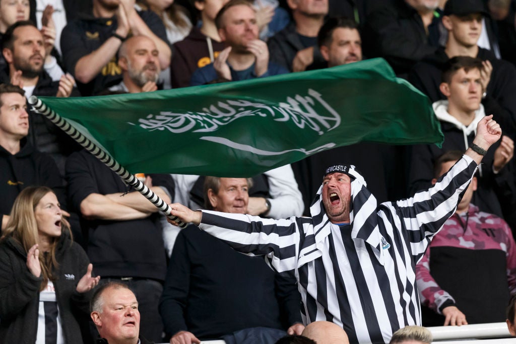 Newcastle fan in black and white Saudi themed dress, waves a Saudi flag